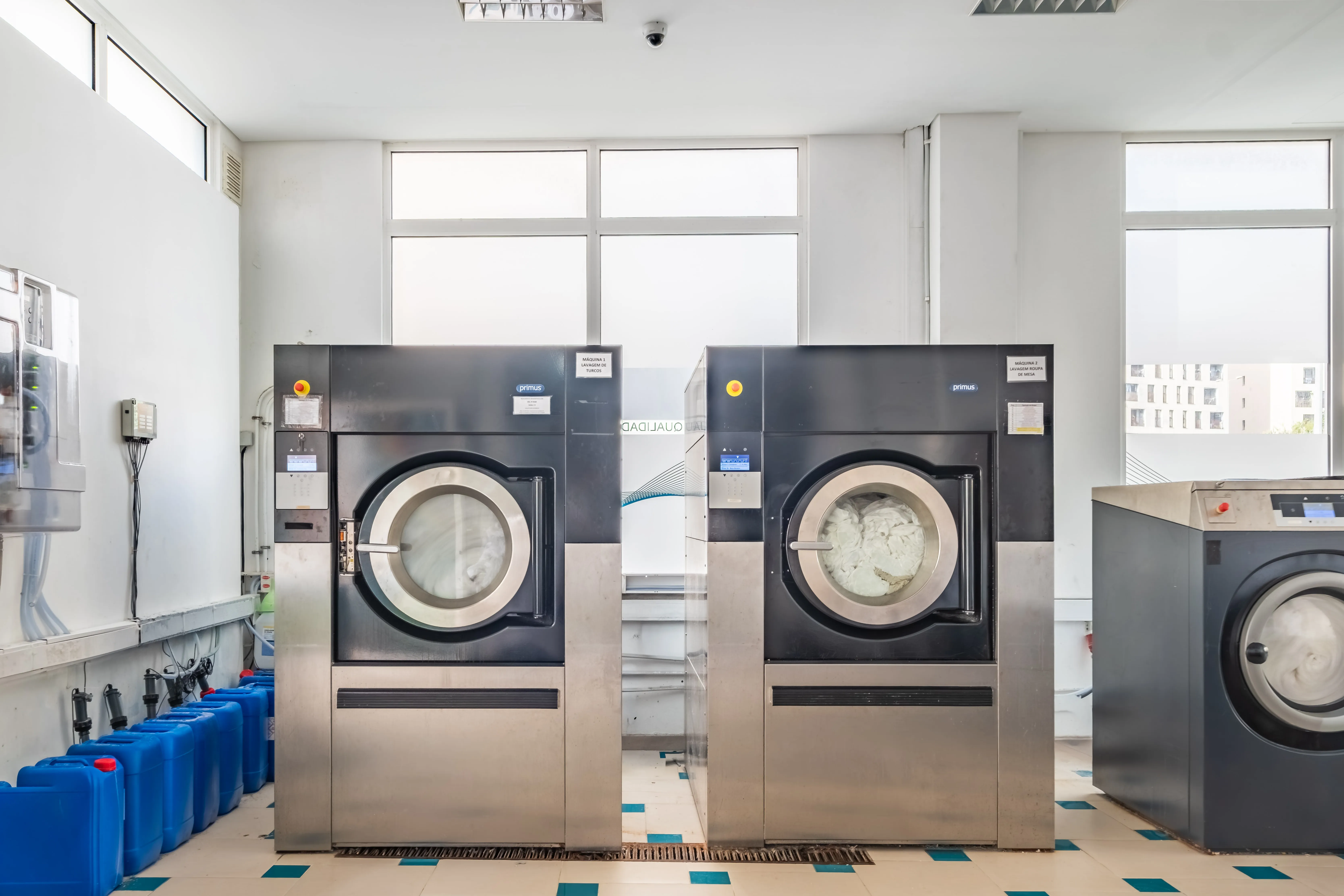 Área de lavagem industrial com equipamentos profissionais para tratamento de grandes volumes de têxteis.