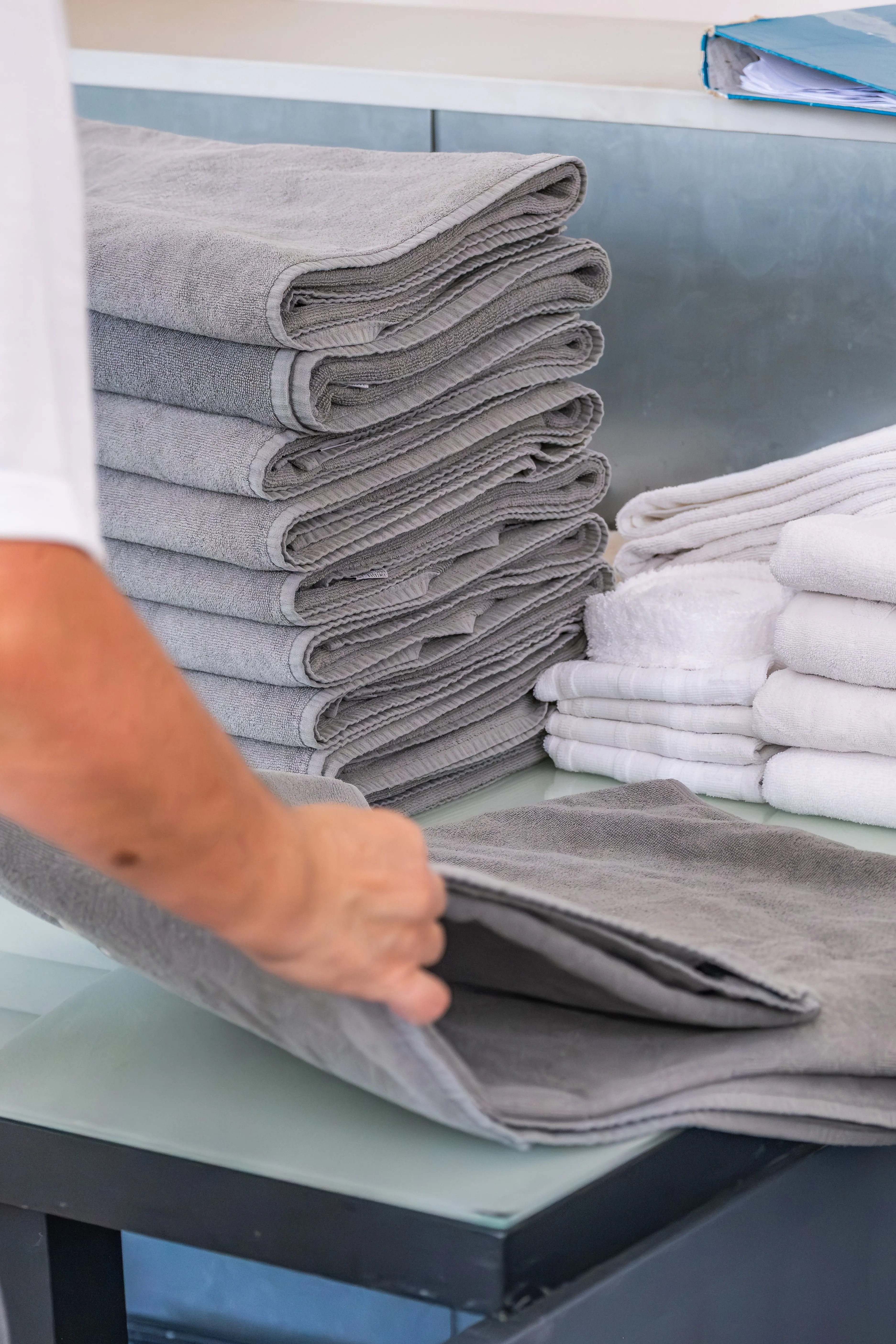 Dobra manual de têxteis profissionais, com pilhas organizadas de toalhas e tecidos tratados com rigor.