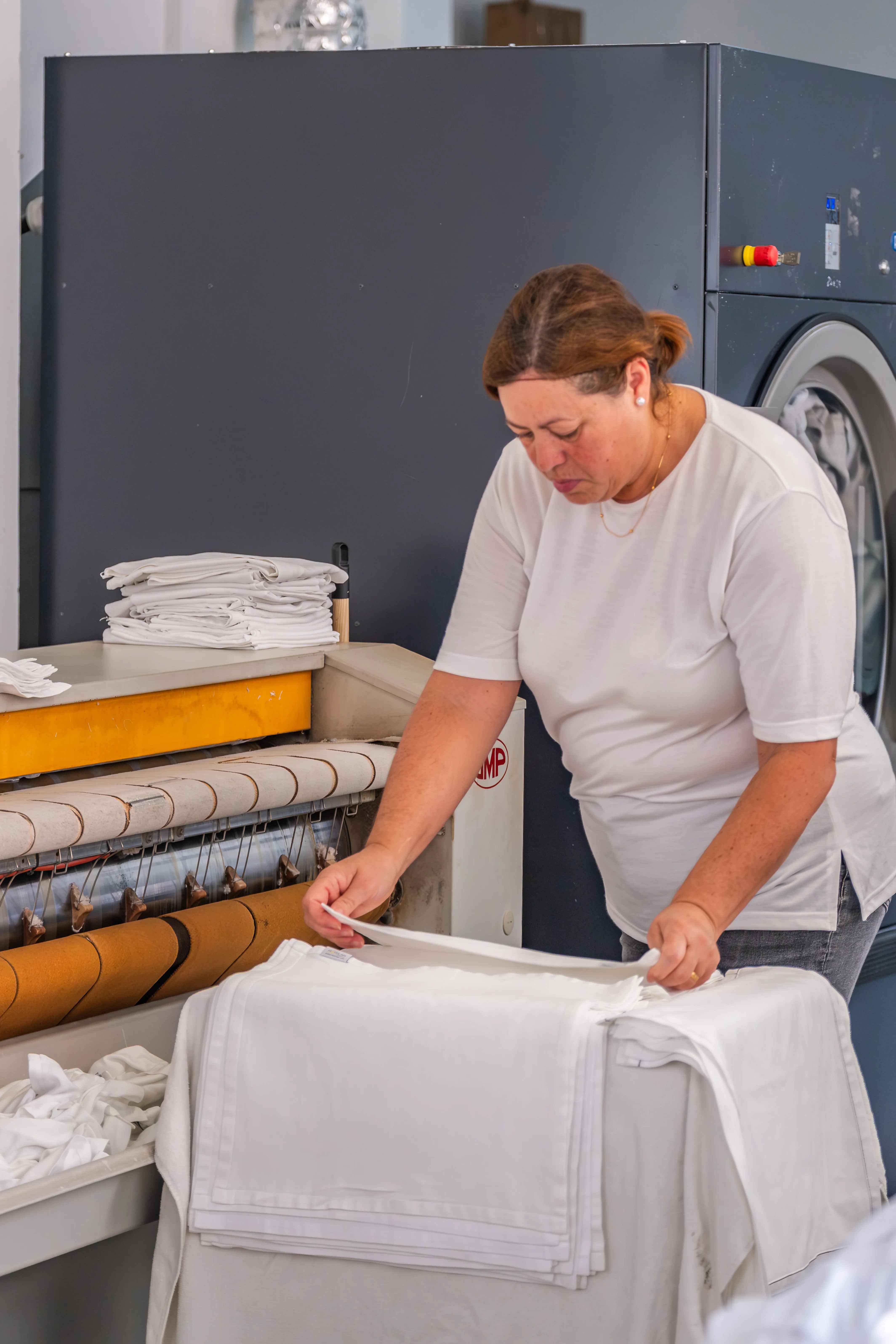 Colaboradora da lavandaria profissional Mãos à Roupa a dobrar e preparar roupa branca em ambiente industrial.