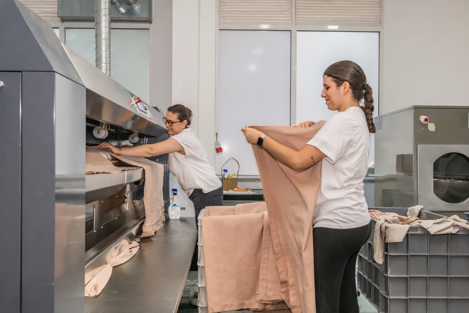 Colaboradoras da lavandaria profissional Mãos à Roupa a dobrar e preparar têxteis em ambiente industrial.
