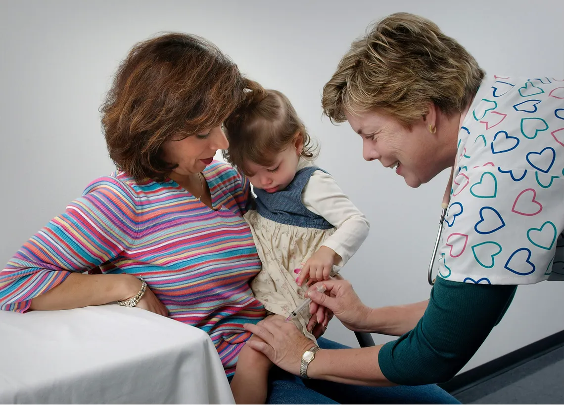A family doctor checking on a small child that is sitting on their mothers lap