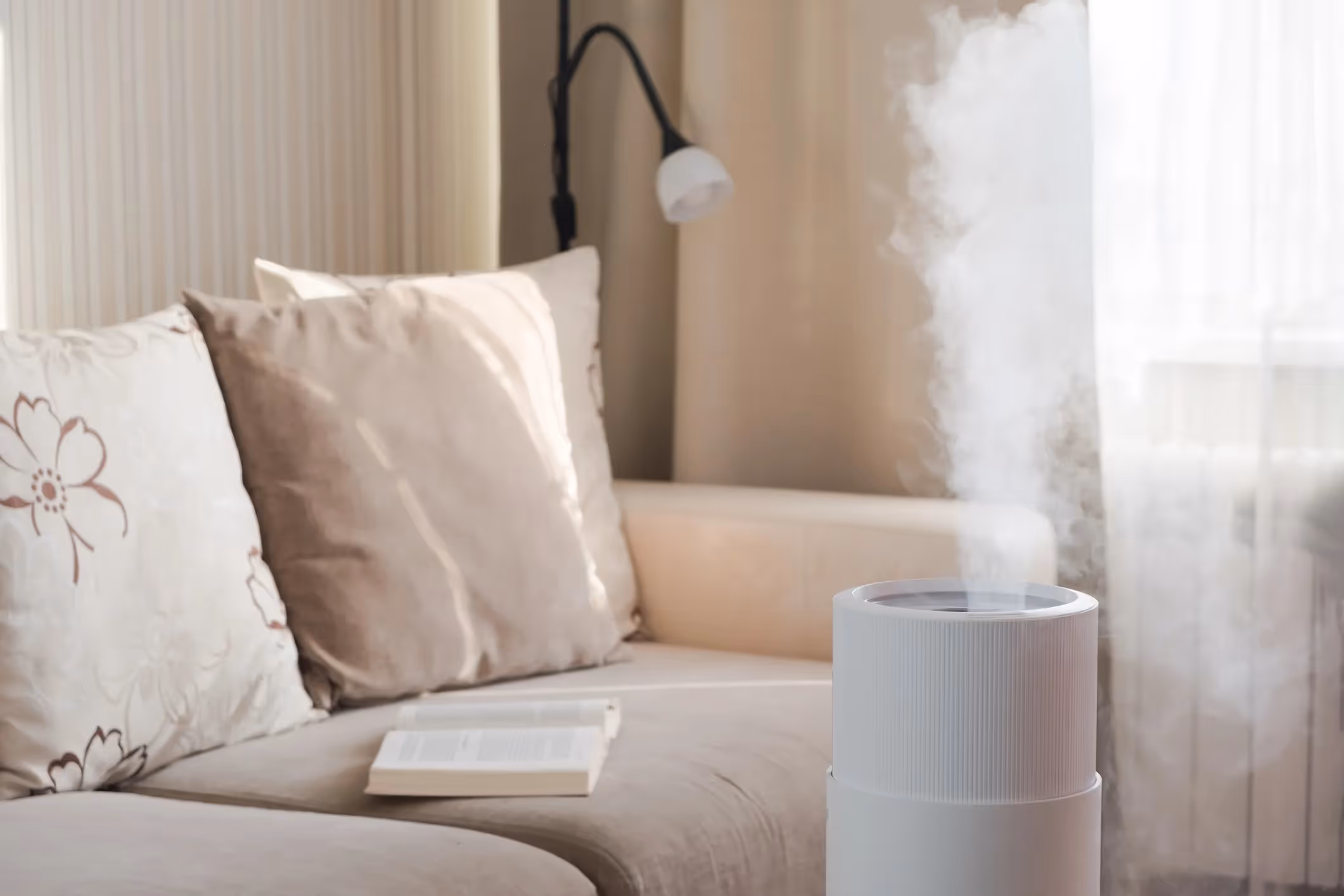 A humidifier is releasing mist in a cozy living room with a beige sofa and a book lying on it.