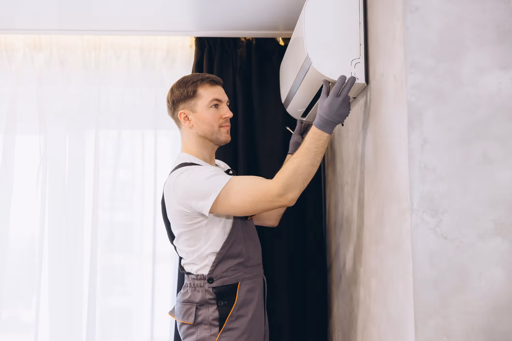 An HVAC technician installing an indoor air conditioning unit on a wall.