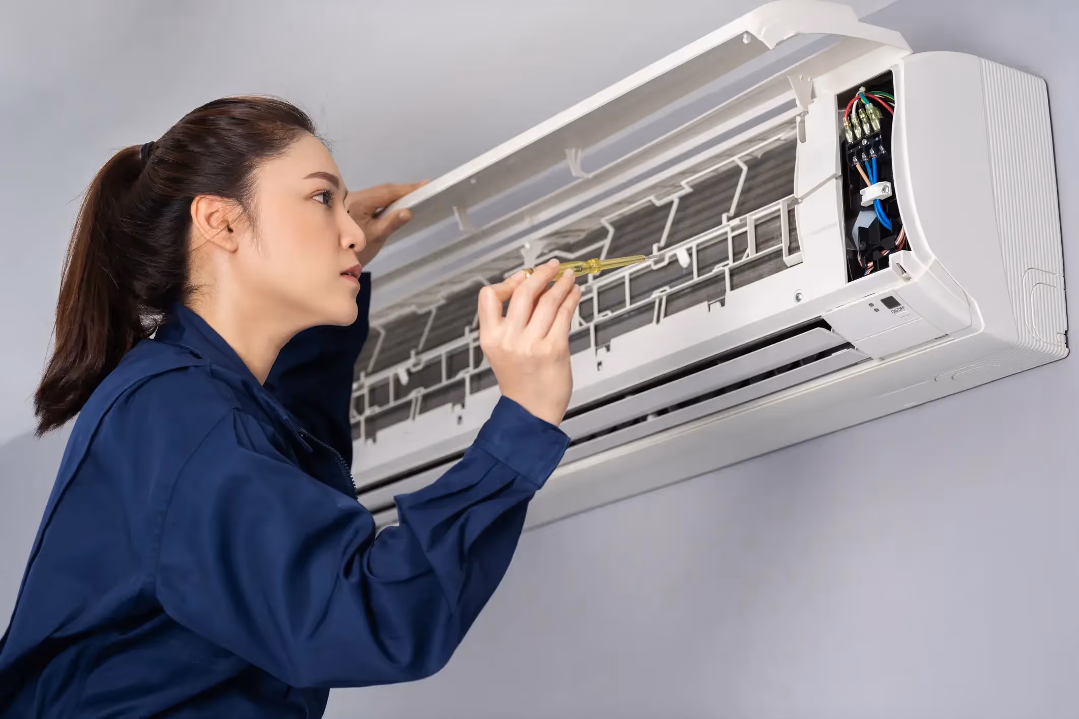 Female HVAC technician servicing an indoor air conditioning unit with a screwdriver.
