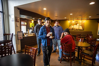 Four people smiling and posing in a warmly lit café with wooden chairs and tables. Chapters Cafe West Valley Church.