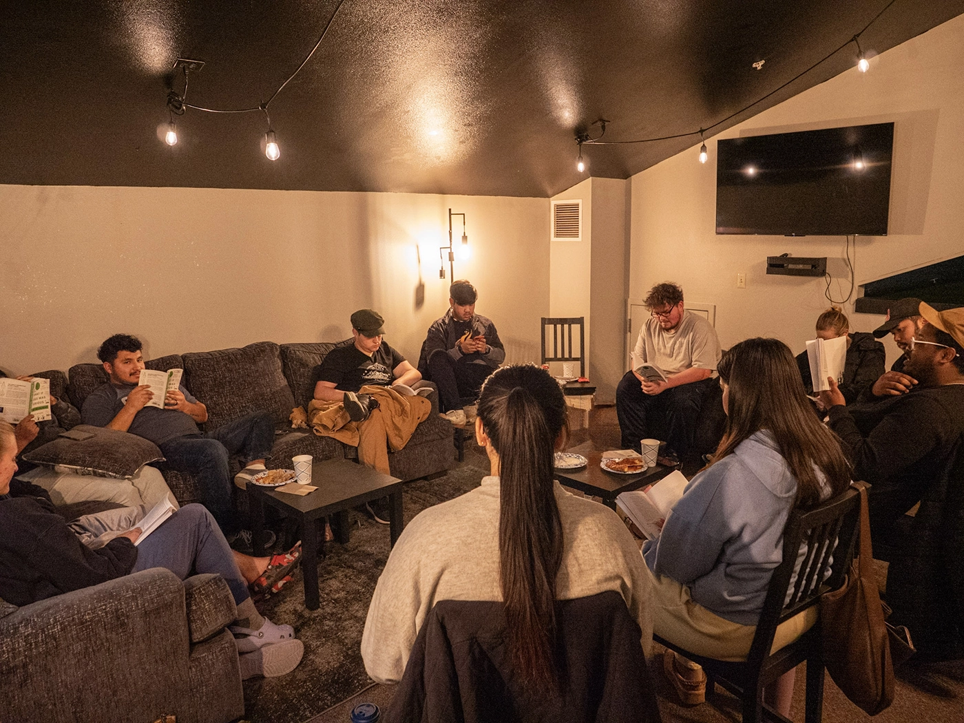 Group of people sitting in a cozy living room reading books and having snacks on tables for Young Adult Life Group at West Valley Church.