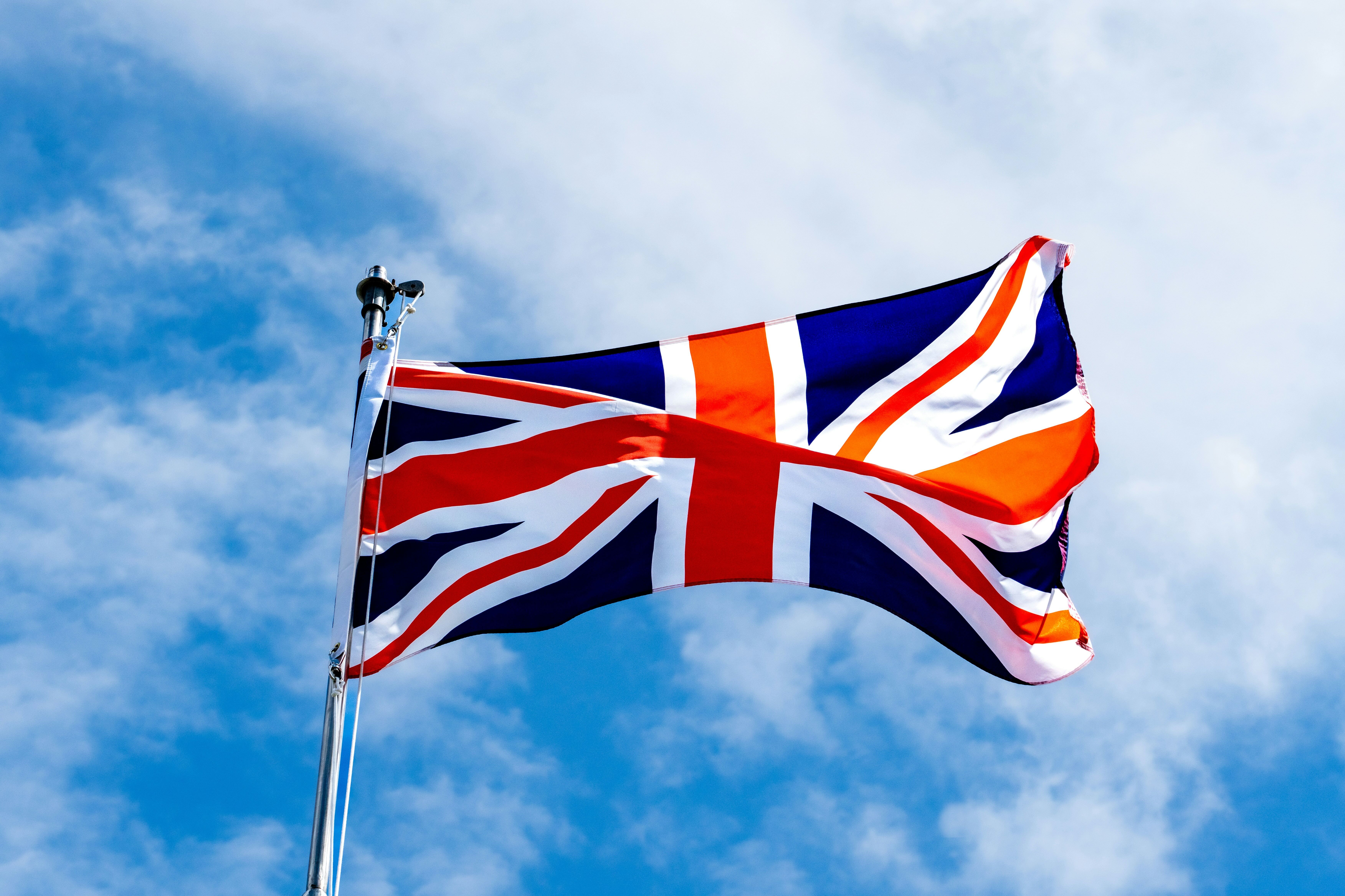 Union Jack flag fluttering on a flagpole against a partly cloudy blue sky.