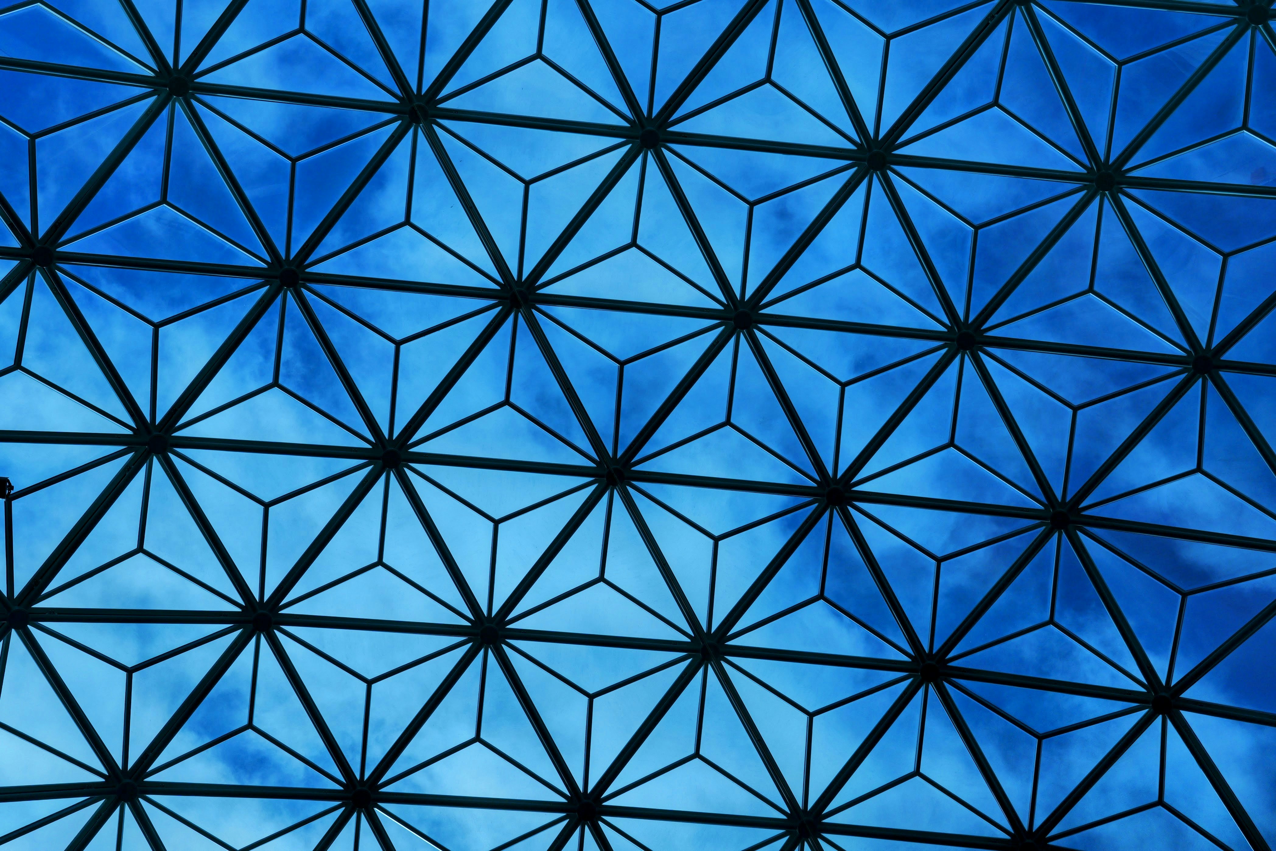Geometric glass ceiling structure with blue sky visible through triangular panes.