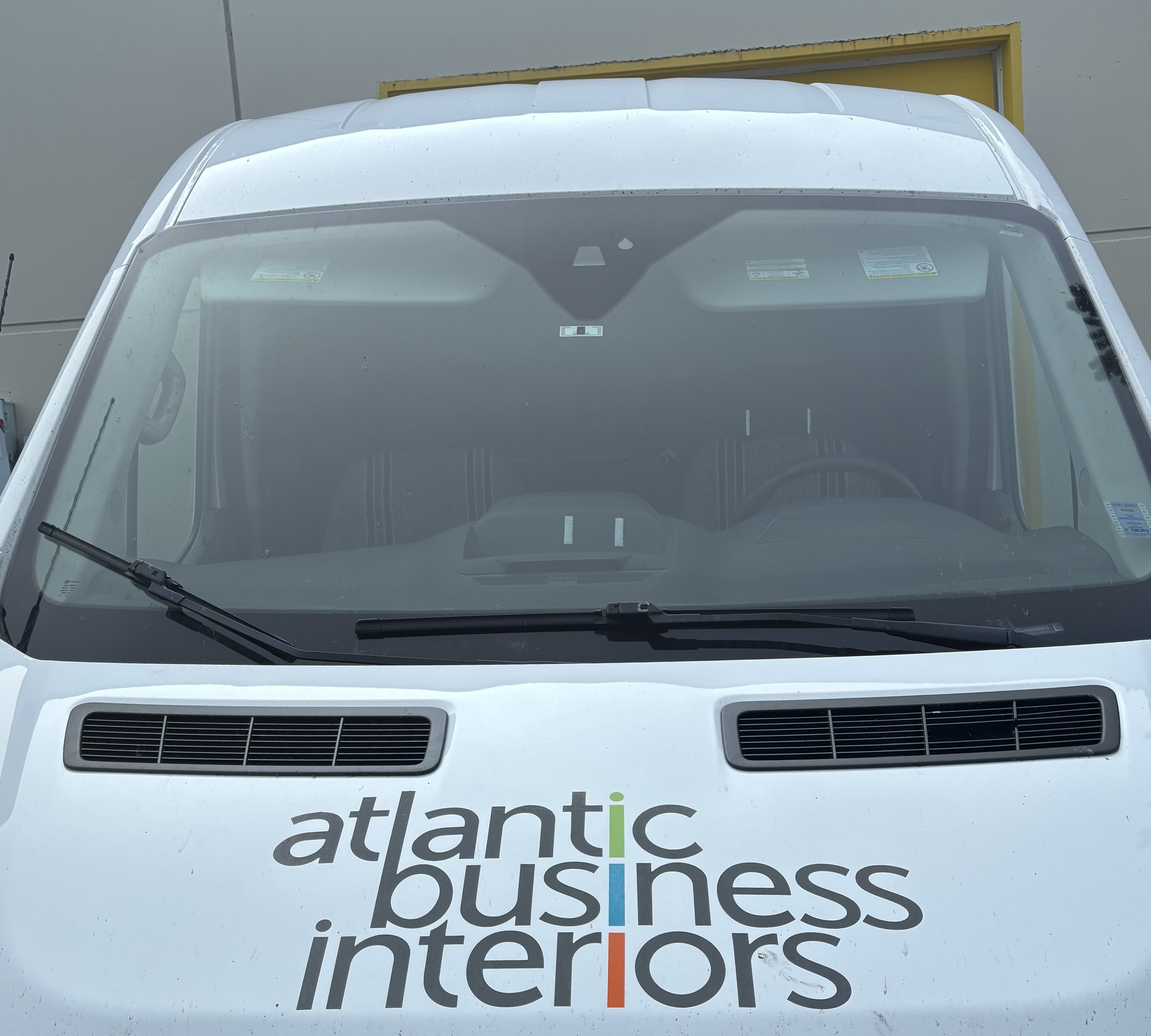 Front windshield and hood of a white vehicle with the logo 'atlantic business interiors' displayed on the hood.