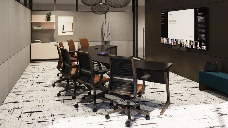 Modern conference room with black table, six office chairs, wall-mounted screen displaying a video call, and patterned carpet.