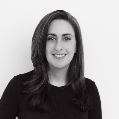 Smiling woman with shoulder-length dark hair wearing a black top against a plain light background.