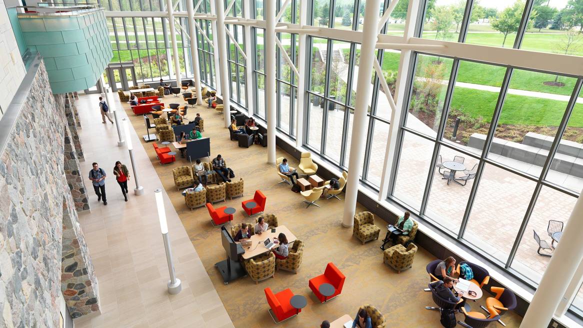 Spacious study area with large floor-to-ceiling windows, various seating arrangements, and people working or walking inside.