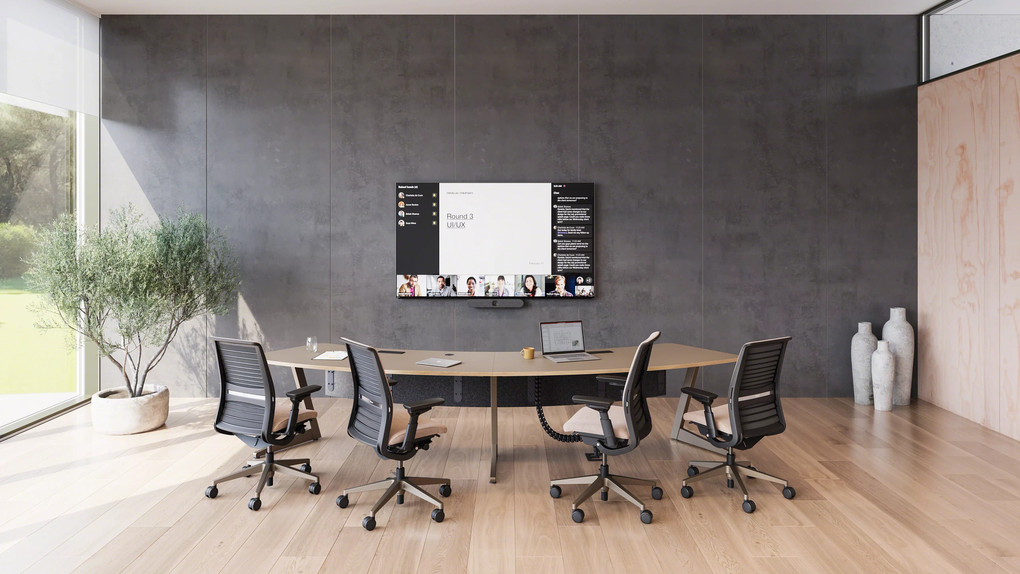 Modern conference room with a curved table, four office chairs, a large wall-mounted screen displaying a virtual meeting, and natural light from floor-to-ceiling windows.