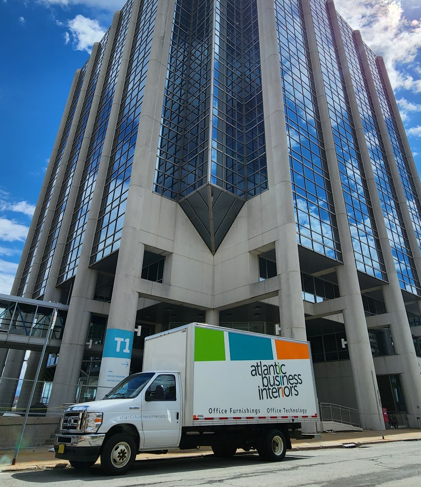 White Atlantic Business Interiors truck parked by a tall modern glass office building under a blue sky.