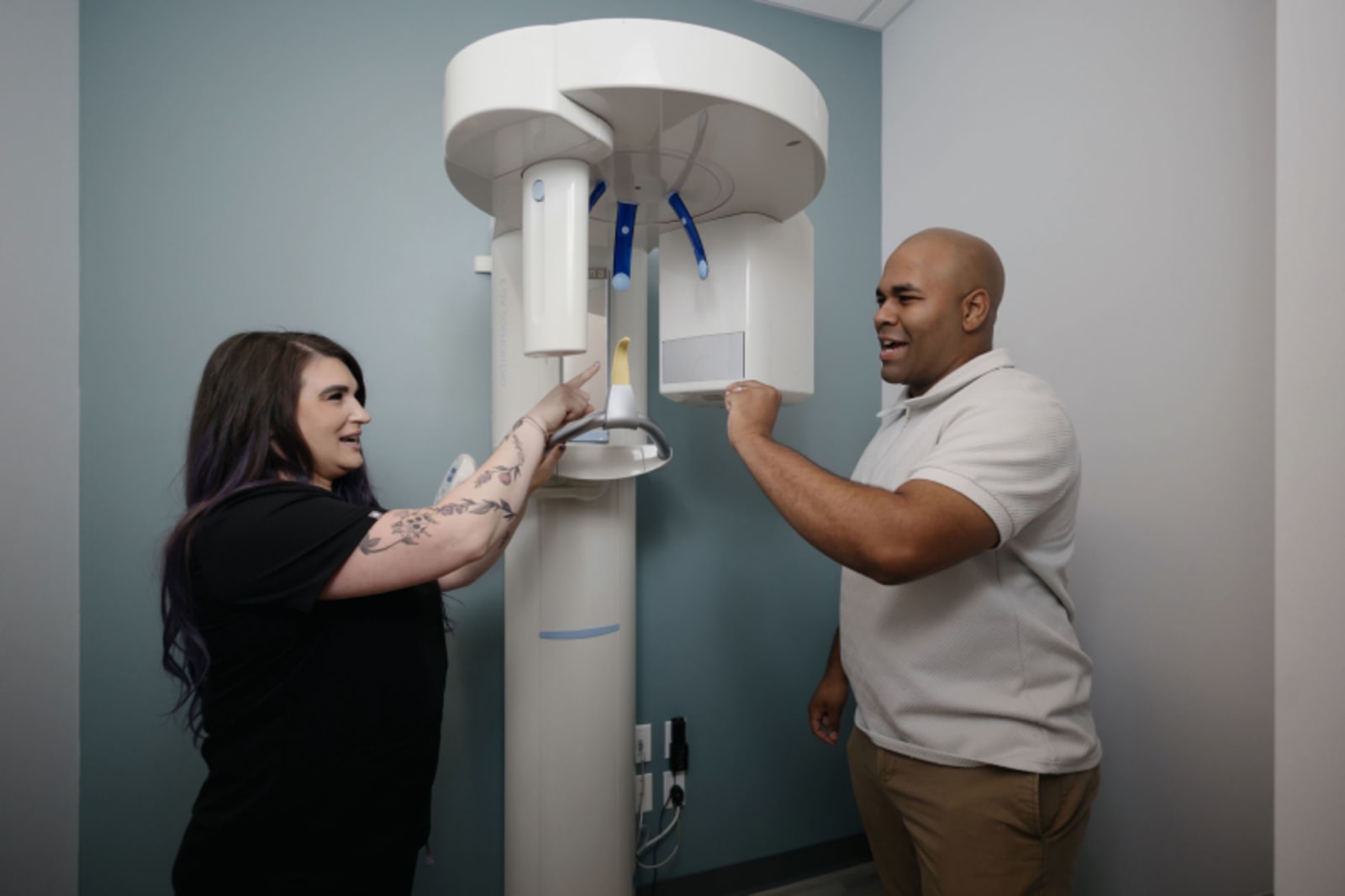 Female dental staff member pointing at digital panoramic X-ray machine while speaking with male colleague in Everett dental o