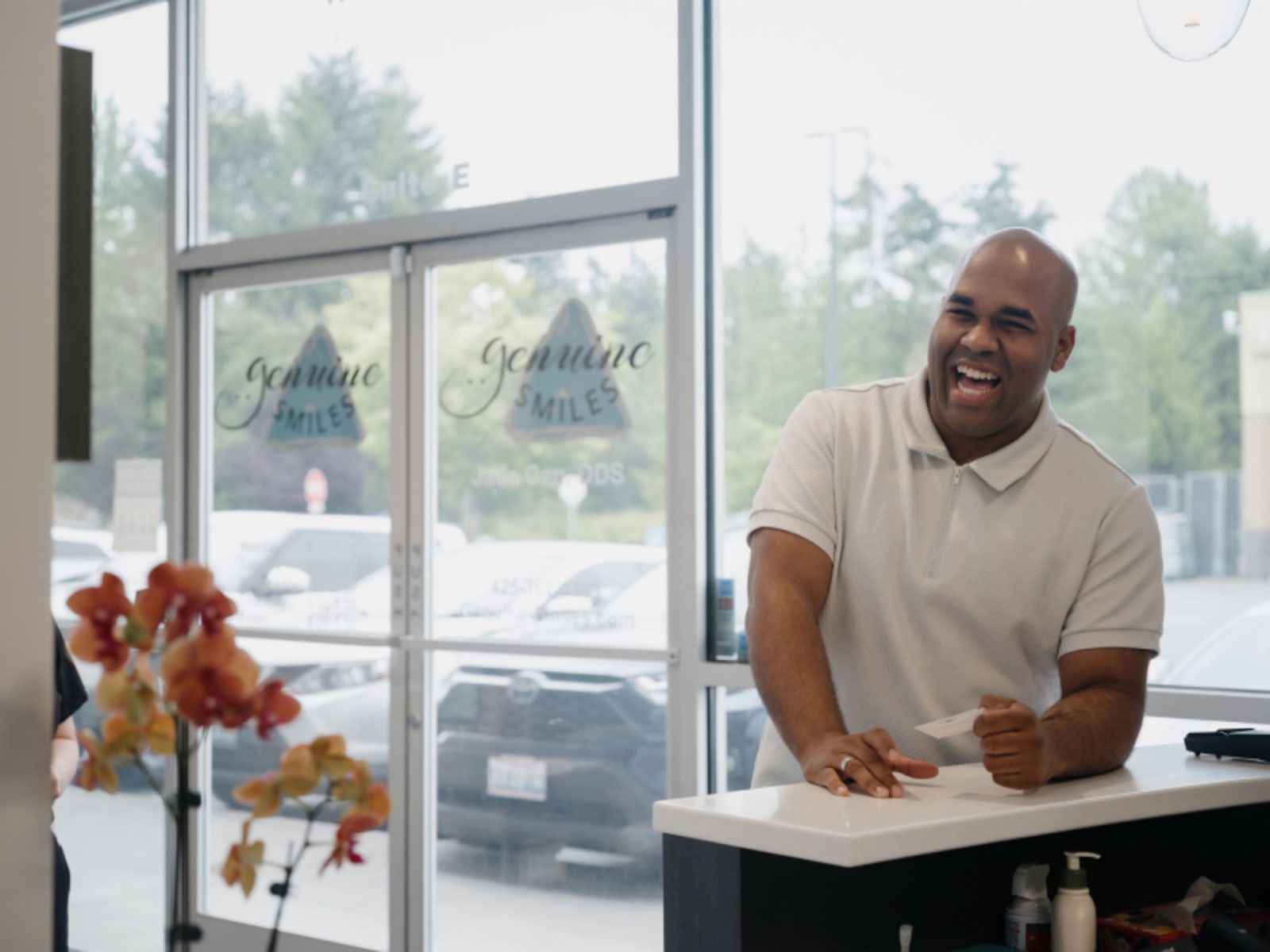 Smiling man in a bright dental office with large windows overlooking trees.