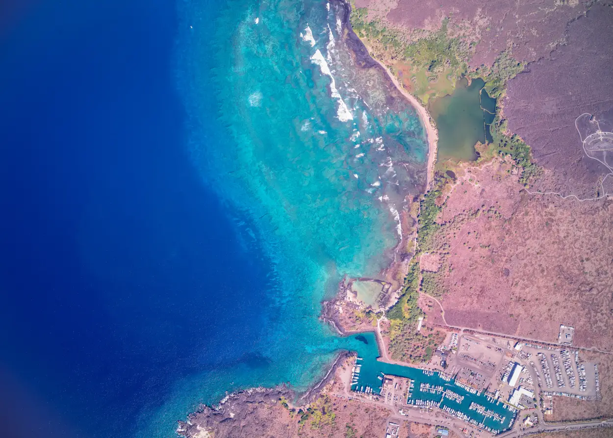 Aerial view of a coastal marina with turquoise shallow waters and deep blue ocean.