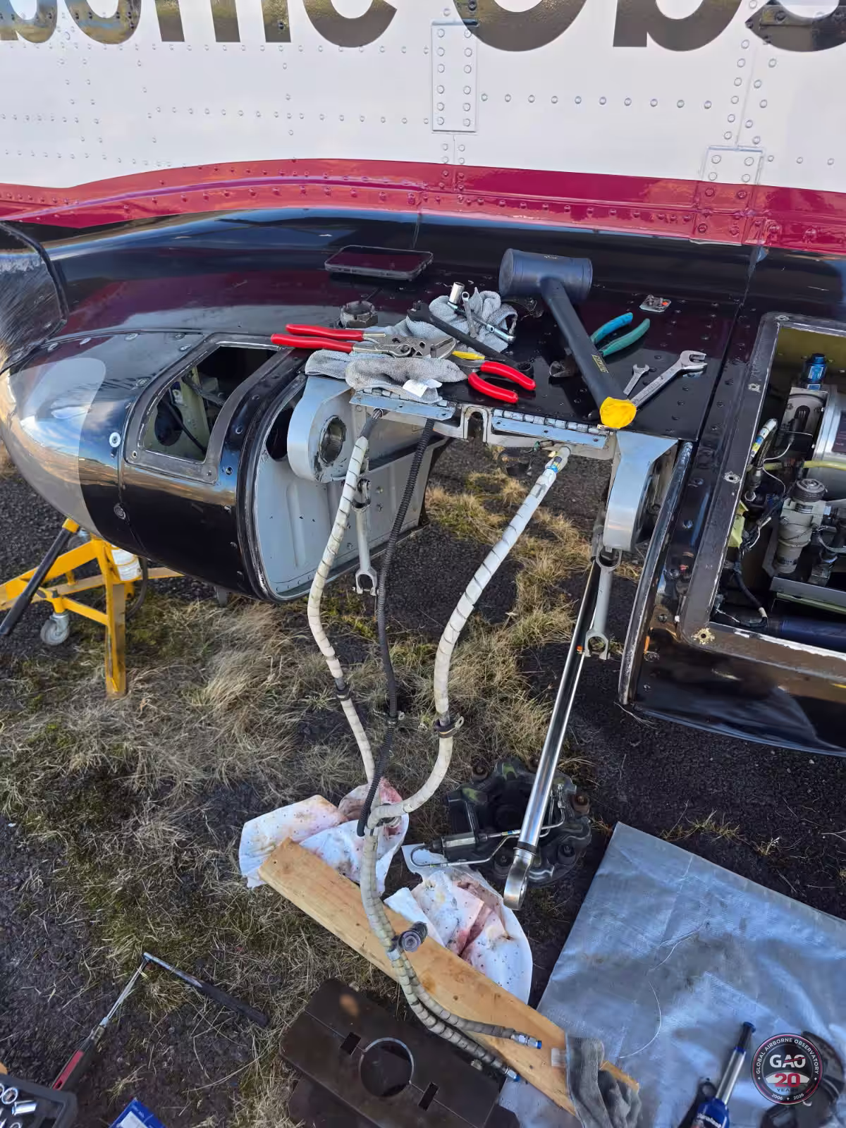 Open aircraft engine compartment with tools and cables hanging out during maintenance on grass.