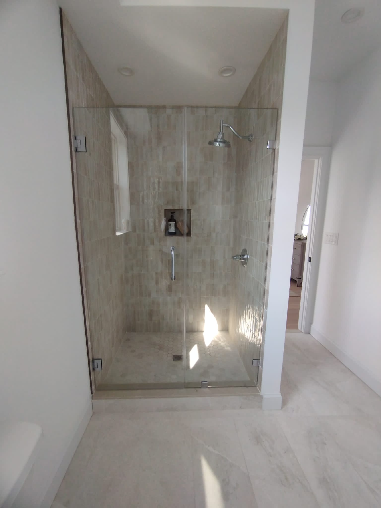 Glass-enclosed shower with beige mosaic tile walls and built-in niche holding a bottle and brush.