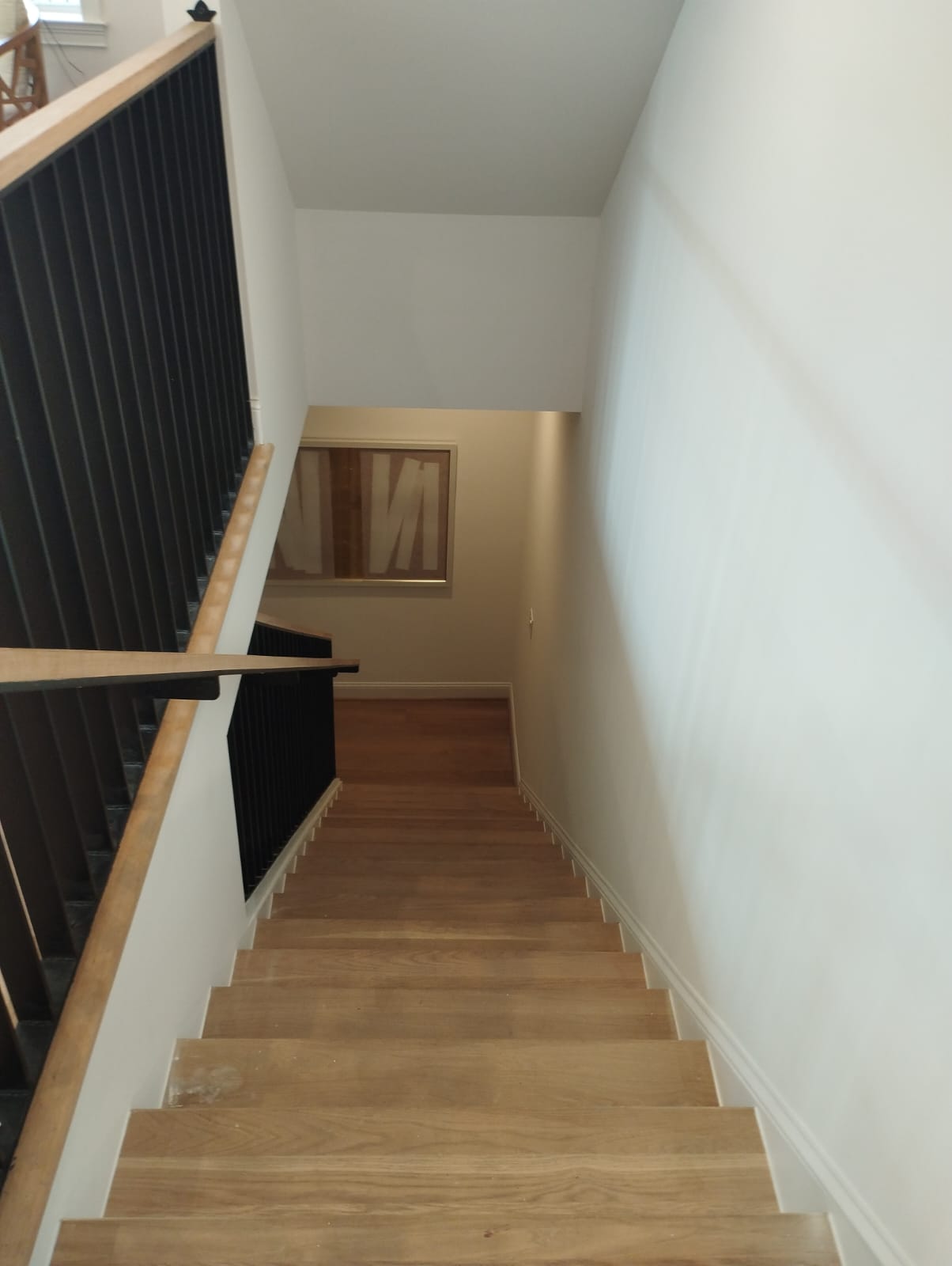 Wooden staircase with black railing descending to a lower floor with a framed abstract artwork on the wall.