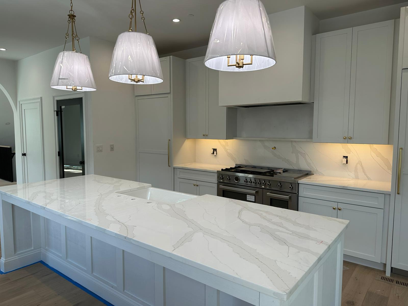 Modern kitchen with white marble countertops, island with sink, stainless steel stove, and three pendant lights.