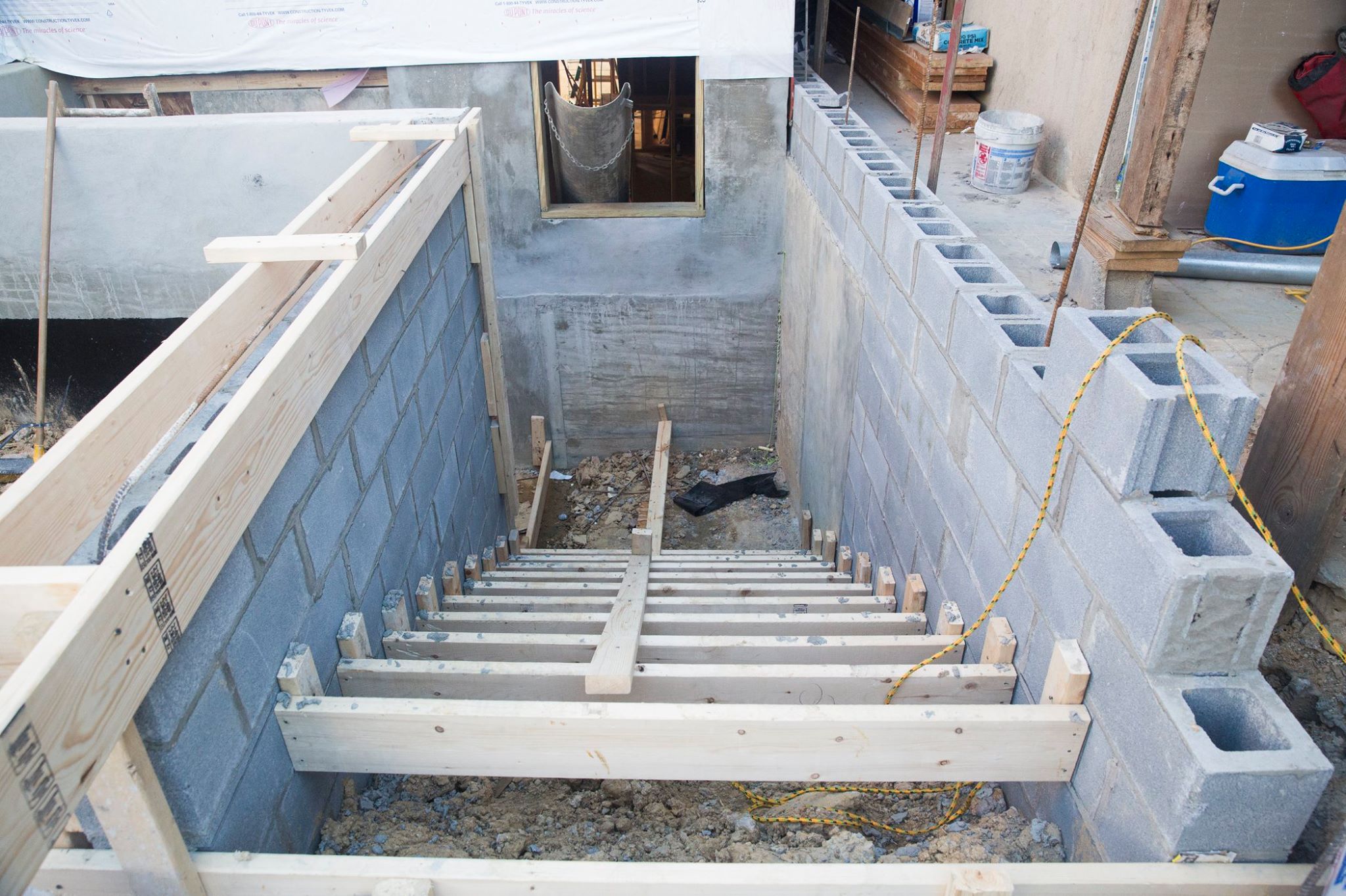 Construction site featuring a stairway under construction with wooden framing and concrete block walls on both sides.