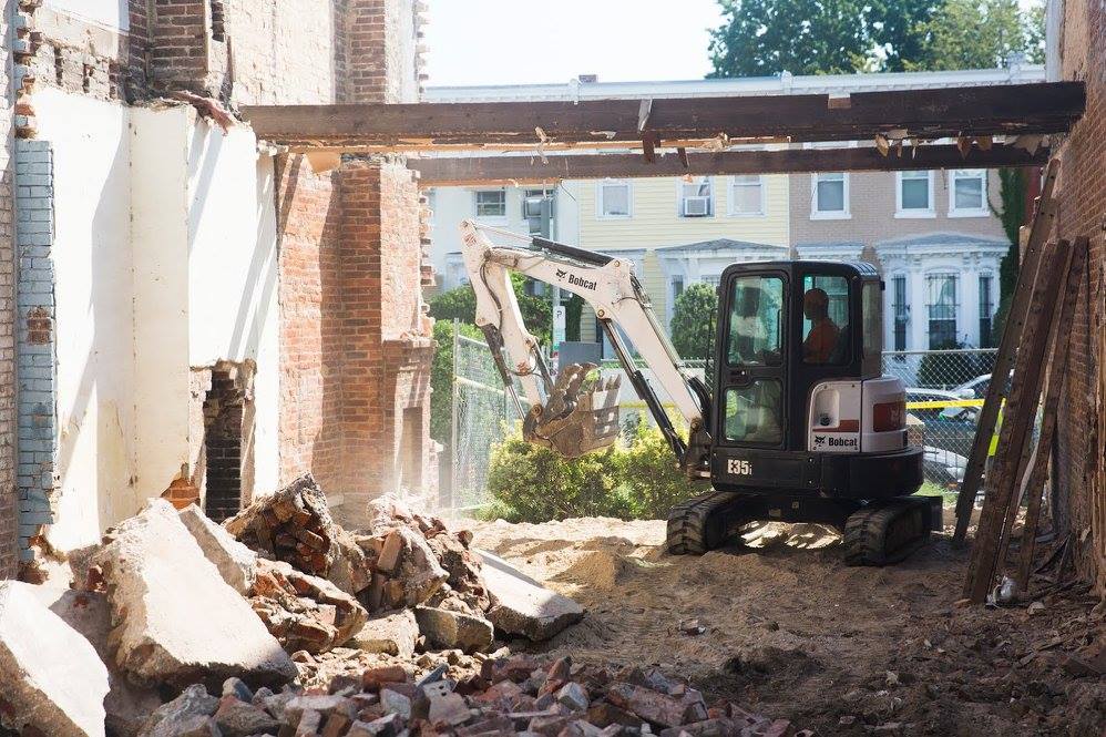 Mini excavator clearing rubble inside a partially demolished brick building under construction.