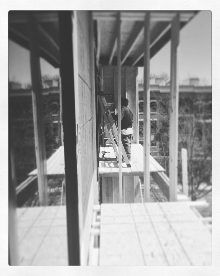 Black and white photo of a person working on scaffolding outside a building under construction.