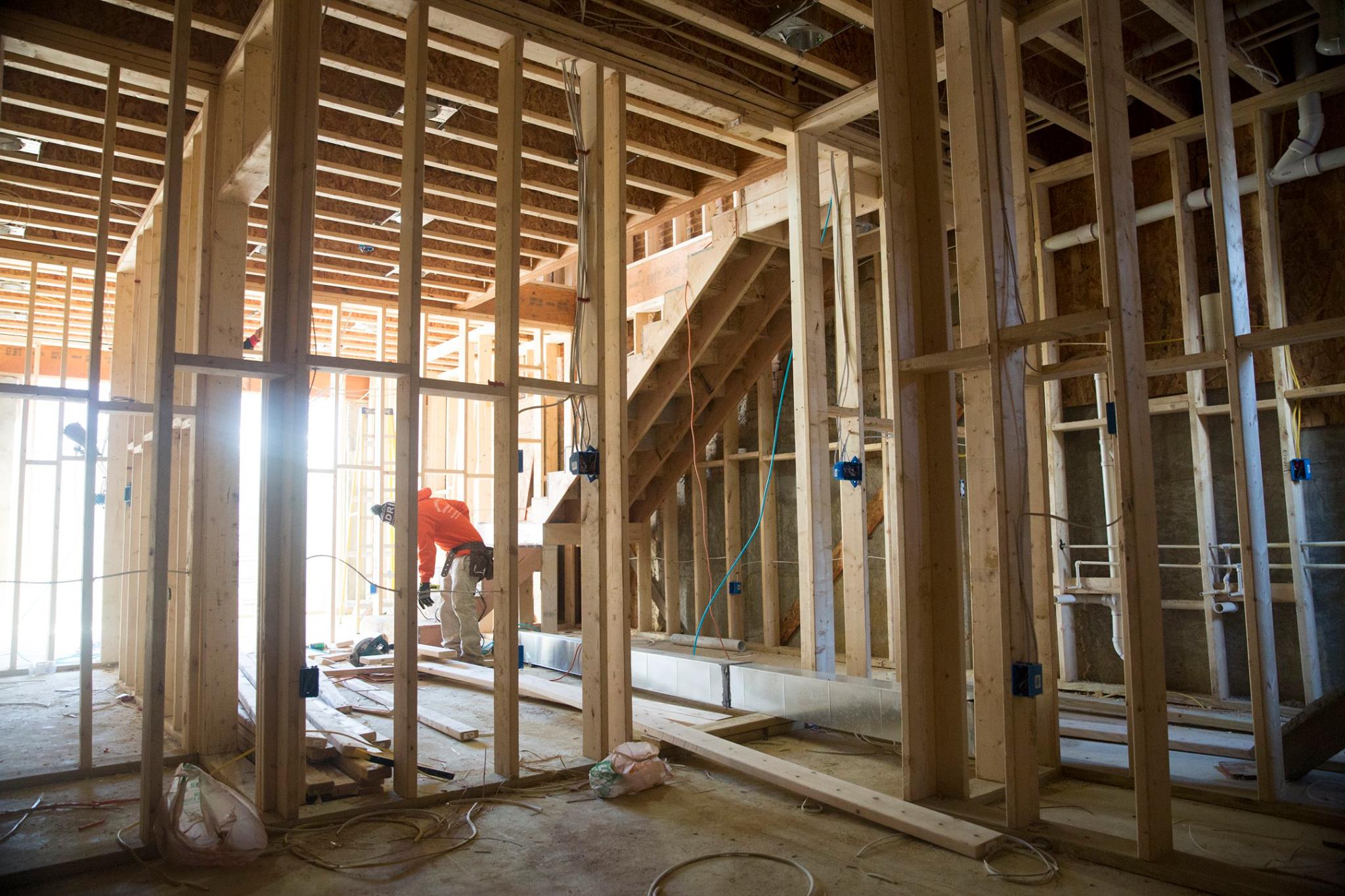 Construction worker in an orange hoodie working inside a wooden frame structure of a building under construction.