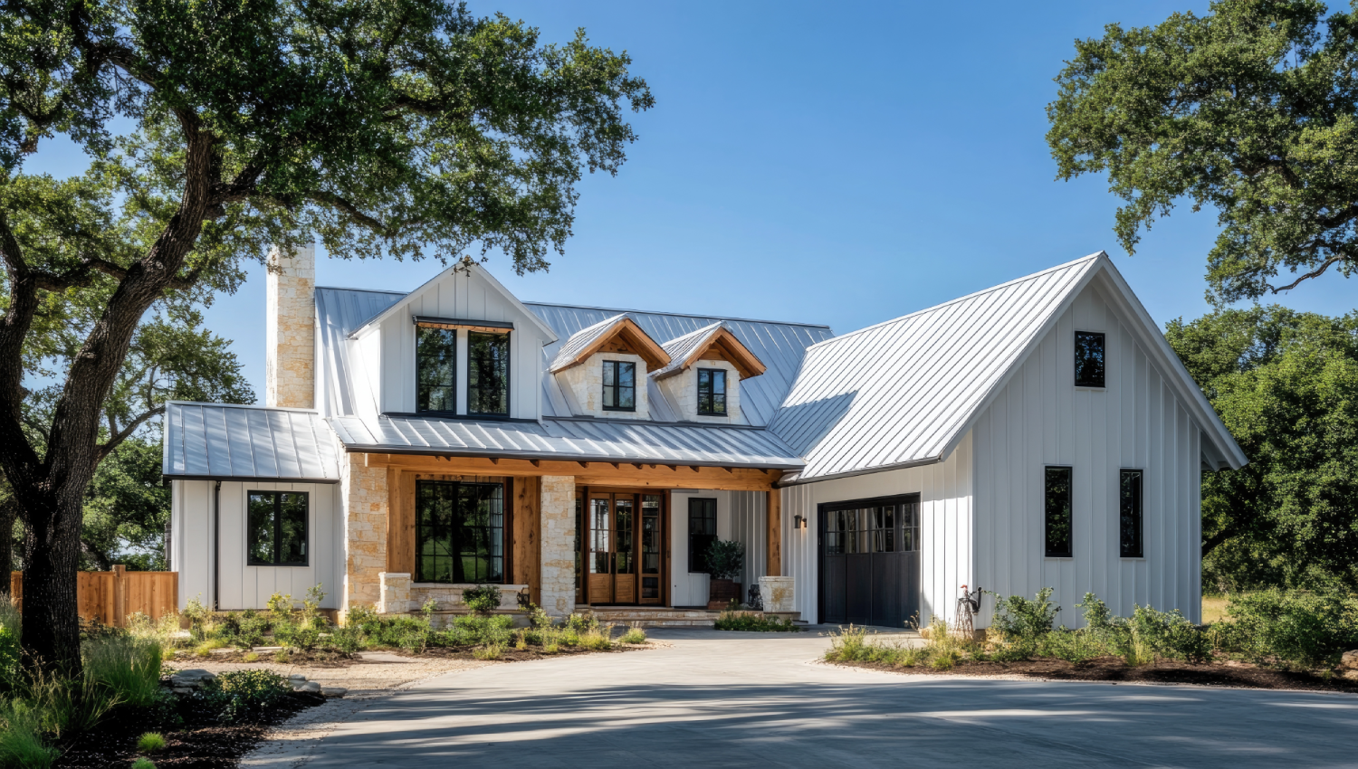 Modern farmhouse with white vertical siding, metal roof, wooden front porch, and large windows, surrounded by trees and greenery.