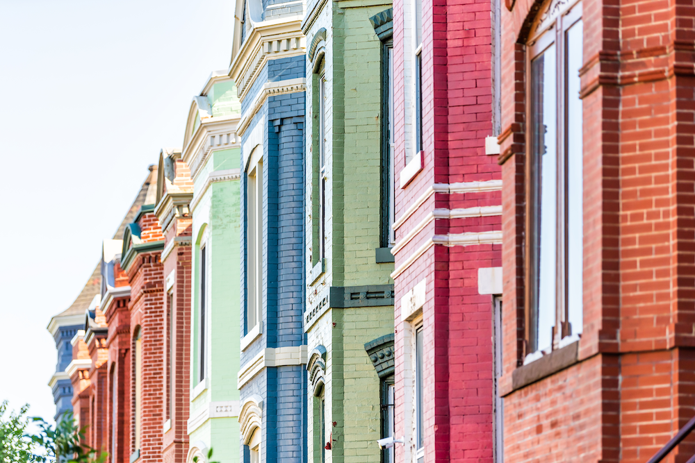 Row of colorful brick townhouses with white-framed windows under a clear sky.