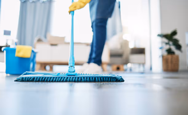 Person mopping a clean tiled floor with a blue mop in a bright living room.