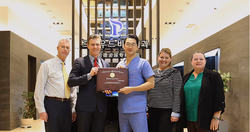 Five people standing in a hallway with one man in a suit and another in medical scrubs holding a certificate.