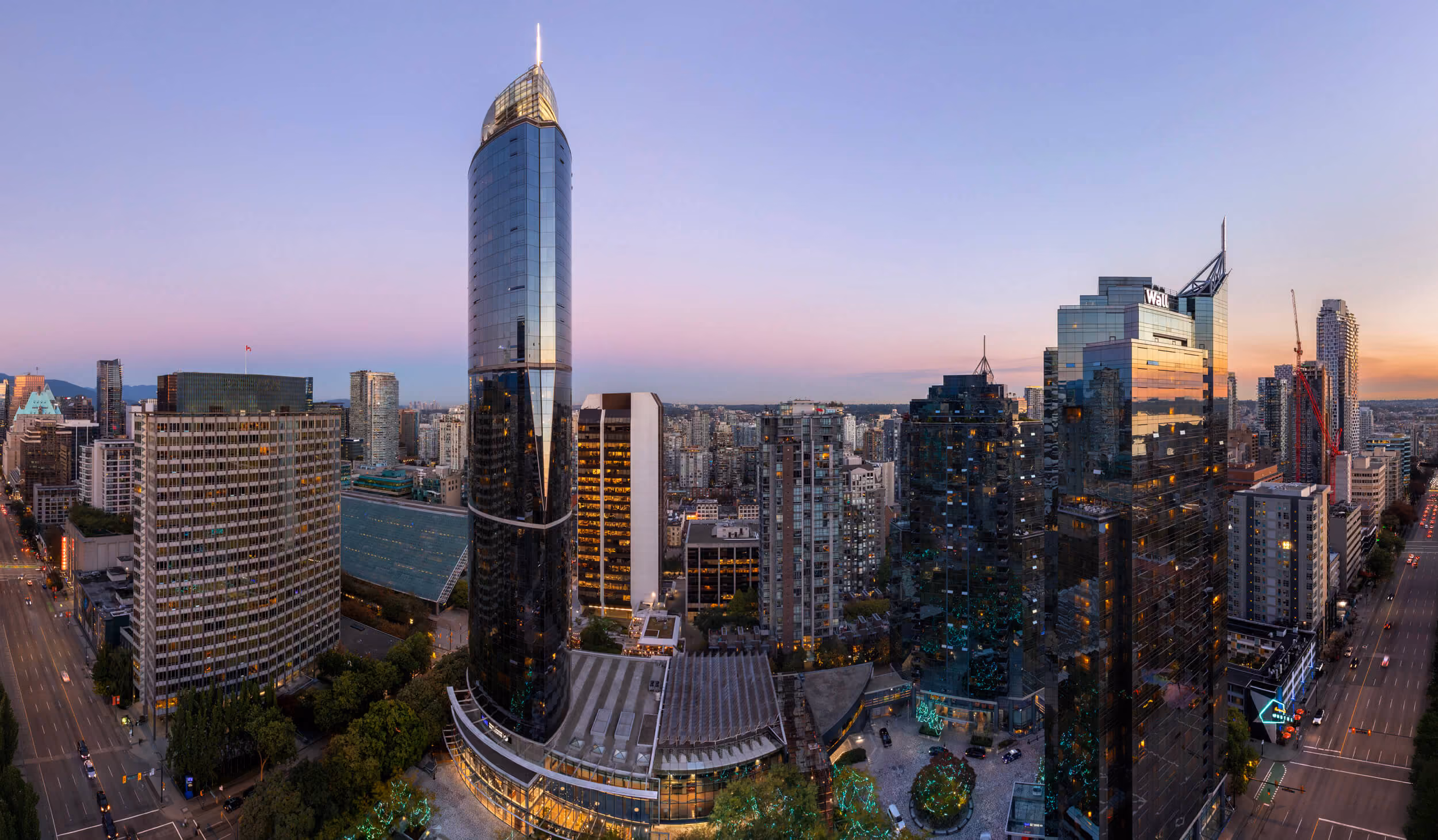 Panoramic cityscape with tall glass skyscrapers at sunset under a clear sky.