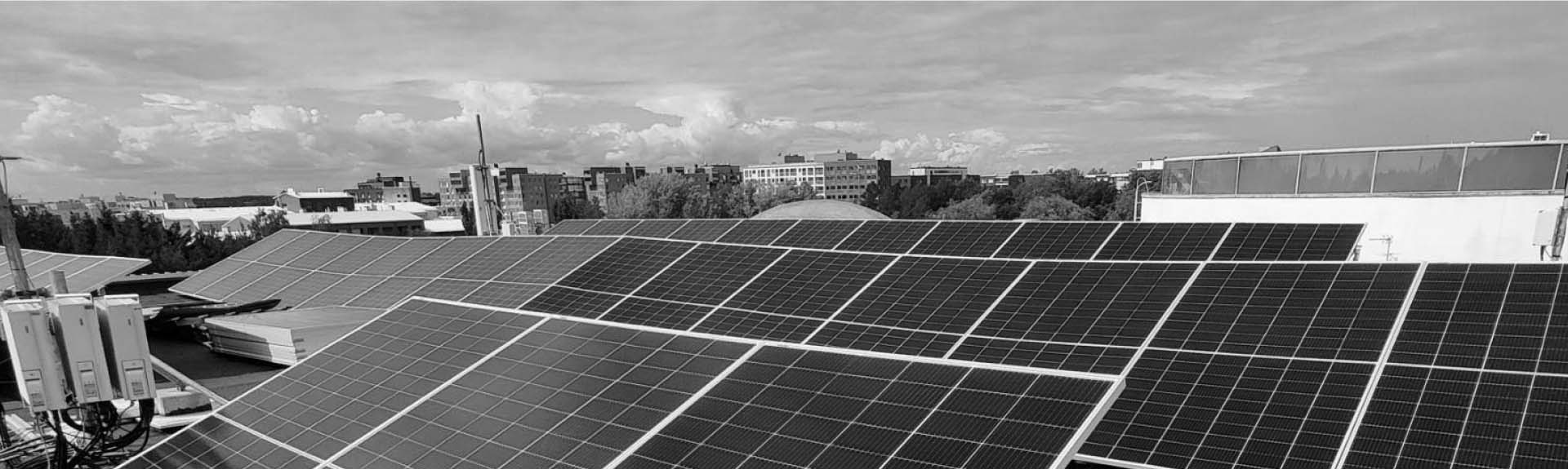 Ralos-aurinkopaneelit asennettuna rakennuksen katolle, taustalla kaupunkimaisema ja pilvinen taivas.