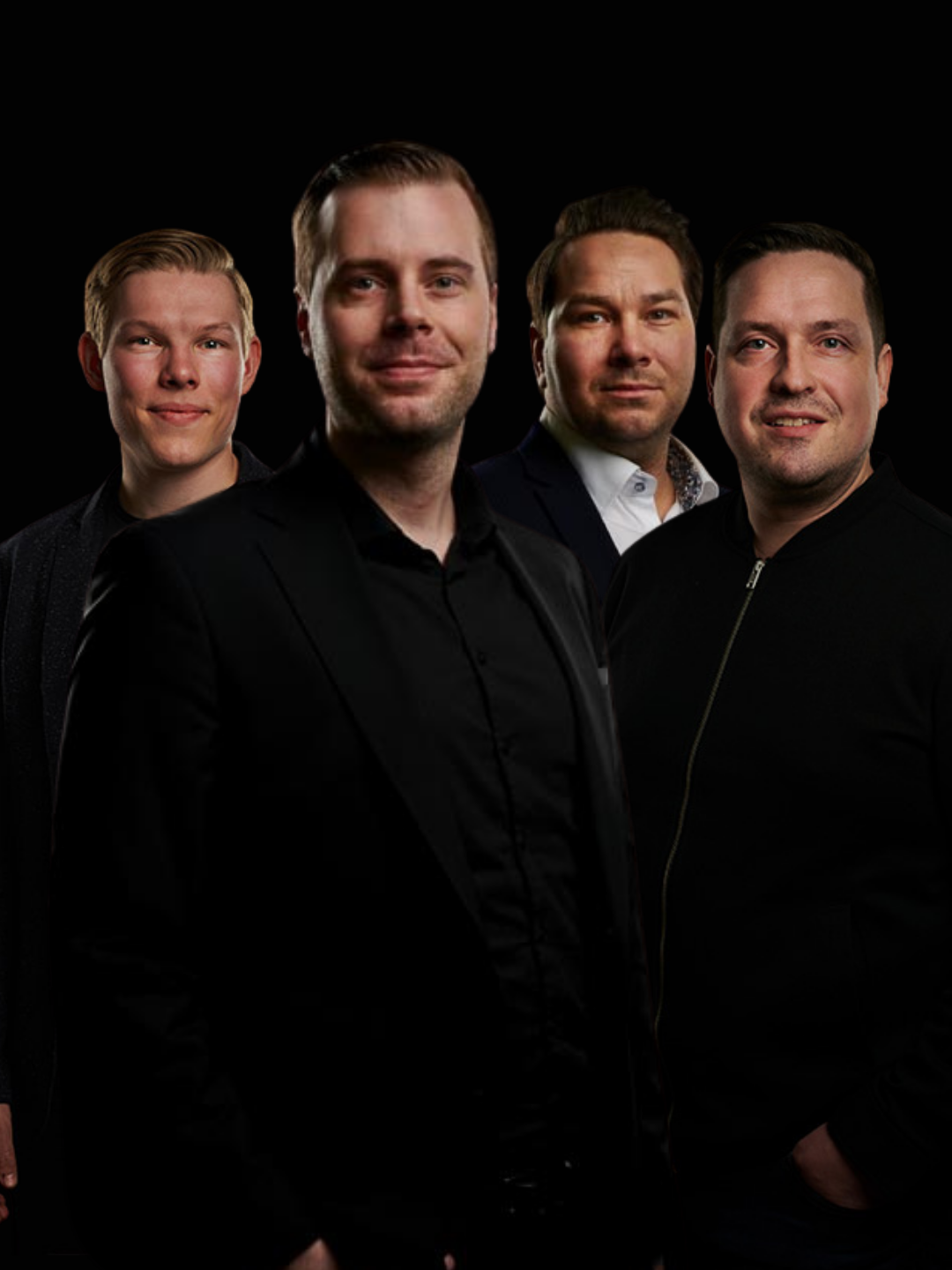 Kuva neljästä Raloksen tiimiläisestä poseeraamassa tummissa vaatteissa mustaa taustaa vasten.