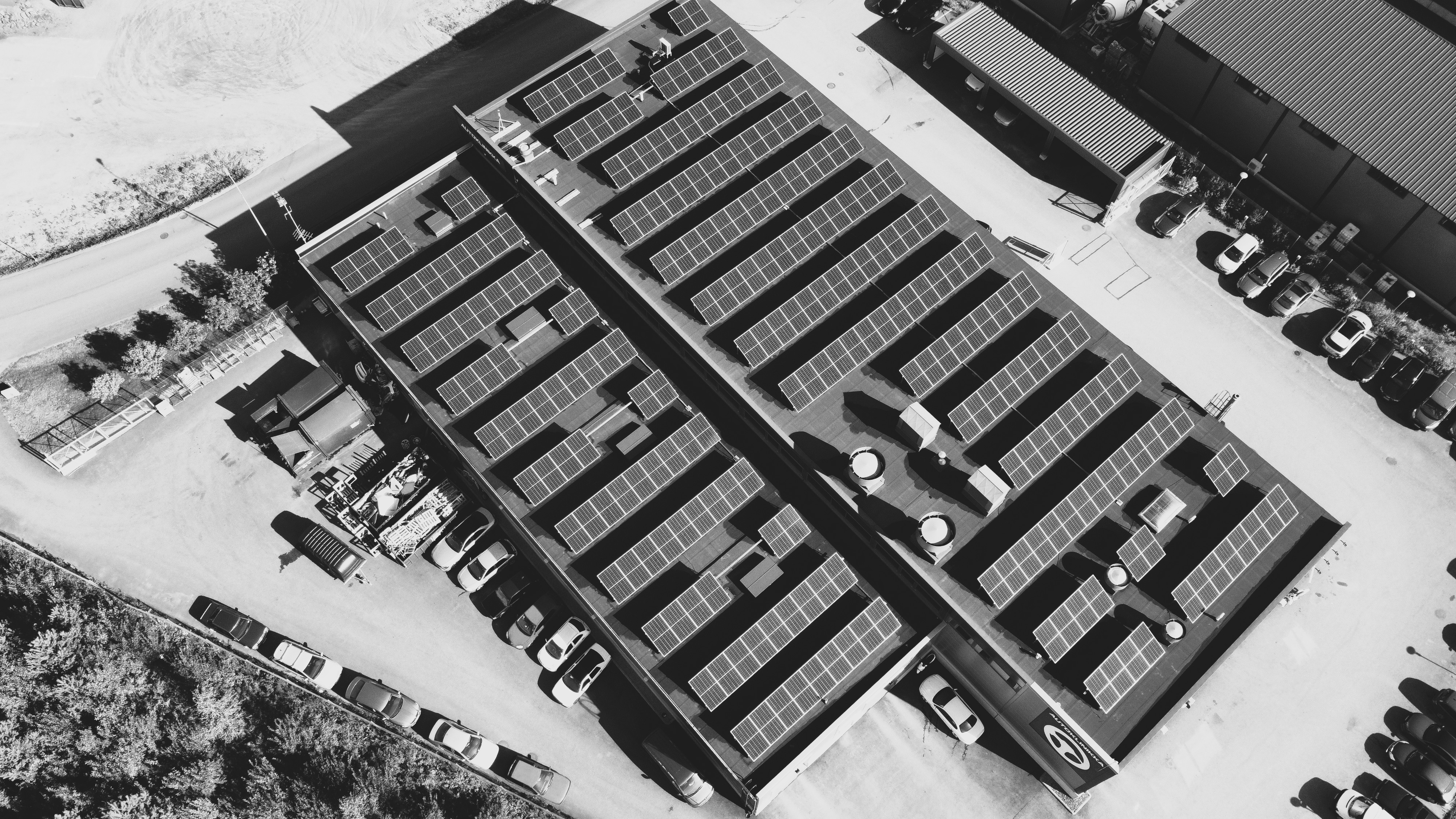 Ilmakuva kahdesta vierekkäisestä tasakatosta, jotka on peitetty Ralos-aurinkopaneeleilla, ympärillä pysäköityjä autoja ja teollisuusrakennuksia.