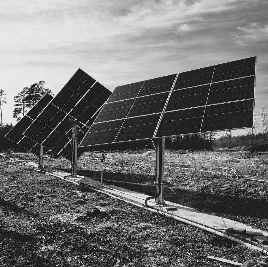 Rivi Ralos-aurinkopaneeleja metallisilla telineillä, taustalla puita pilvisen taivaan alla.