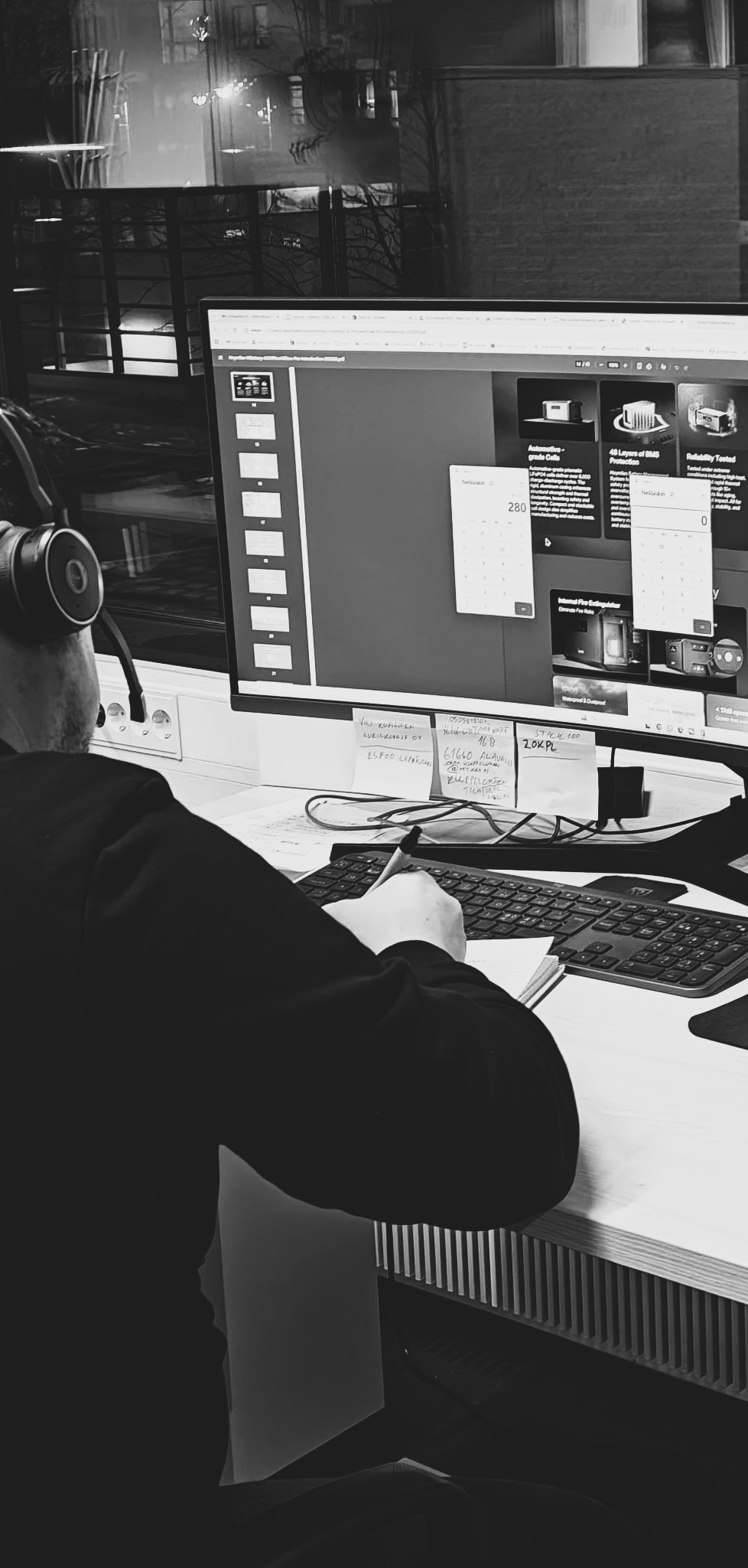 Henkilö kuulokkeet päässä tekemässä muistiinpanoja tietokonepöydän ääressä, suurella näytöllä verkkosivu ja laskinsovellus.