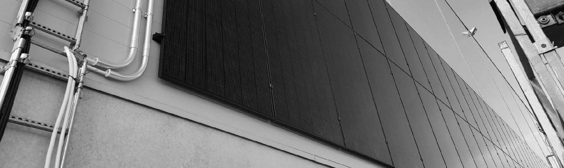 Mustavalkoinen lähikuva Ralos-aurinkopaneeleista rakennuksen ulkoseinällä.