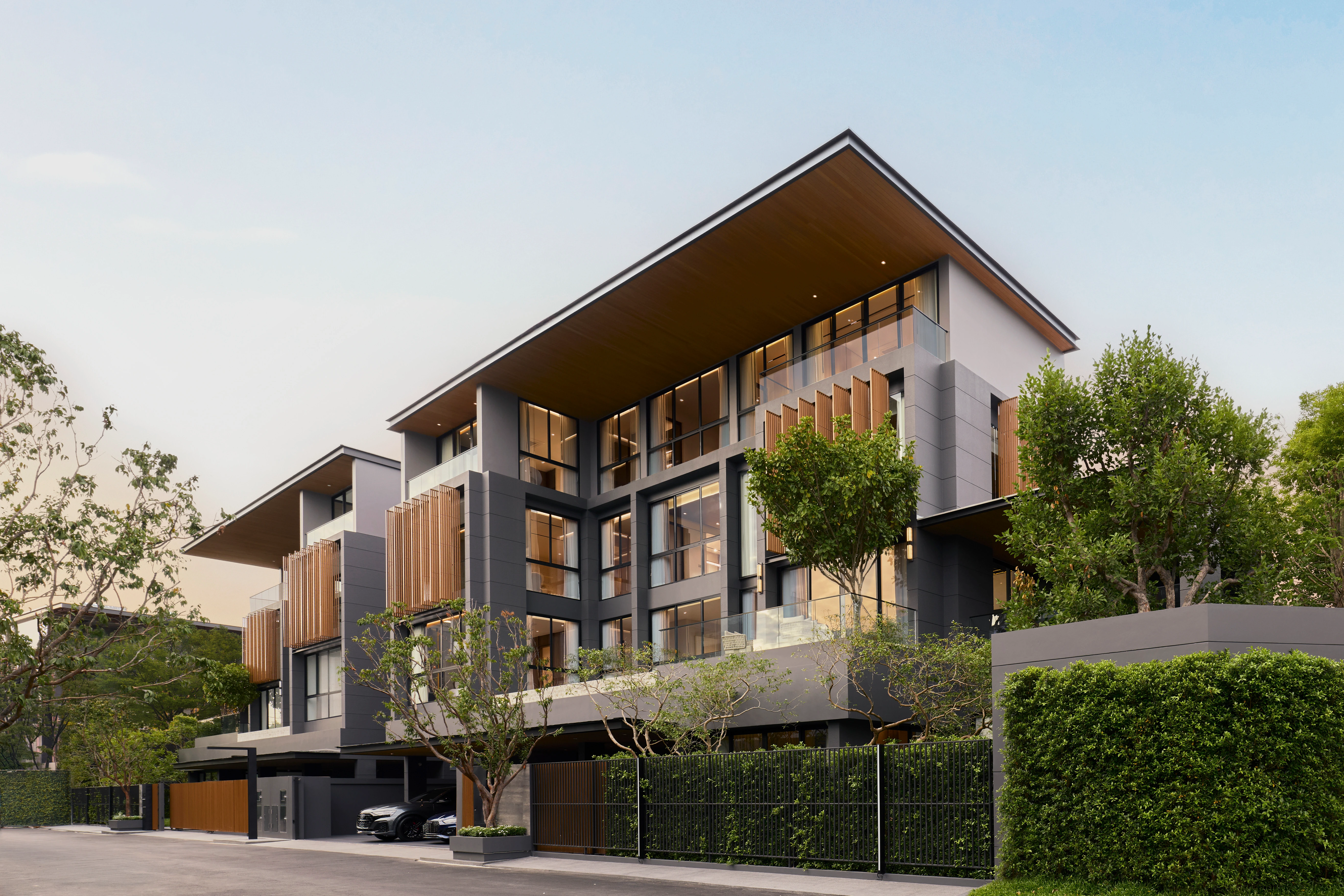 Modern multi-story house with large glass windows, wood accents, greenery, and luxury cars parked in front.