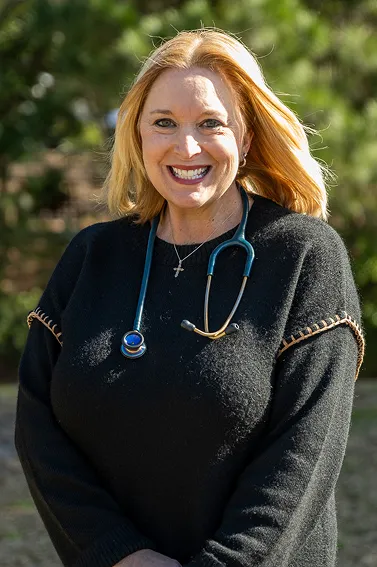 Smiling woman with blonde hair wearing a black sweater and a stethoscope around her neck outdoors.