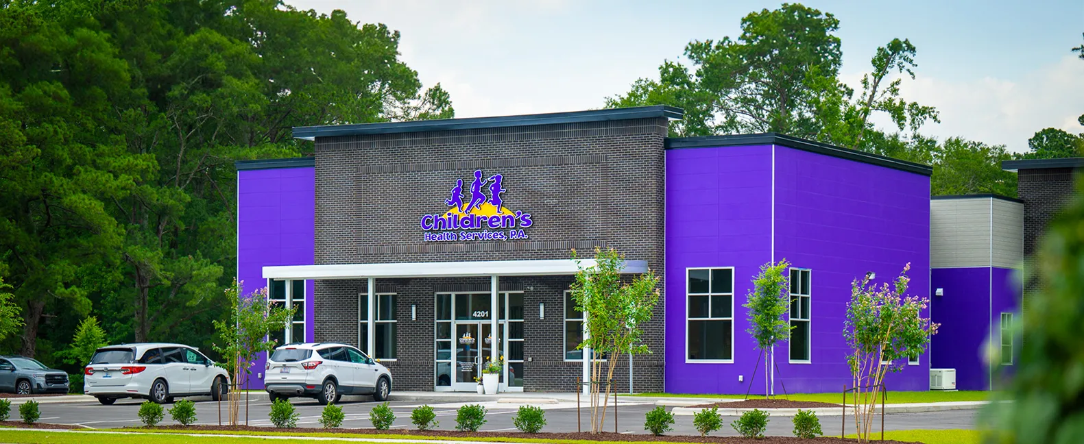 Modern building with purple walls and brick facade labeled 'Children’s Health Services, P.A.' with parked cars and trees nearby.