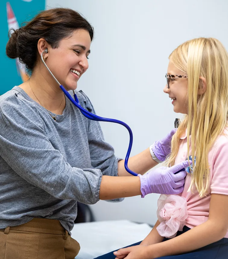 Female doctor using a stethoscope on a smiling young girl during a medical checkup.
