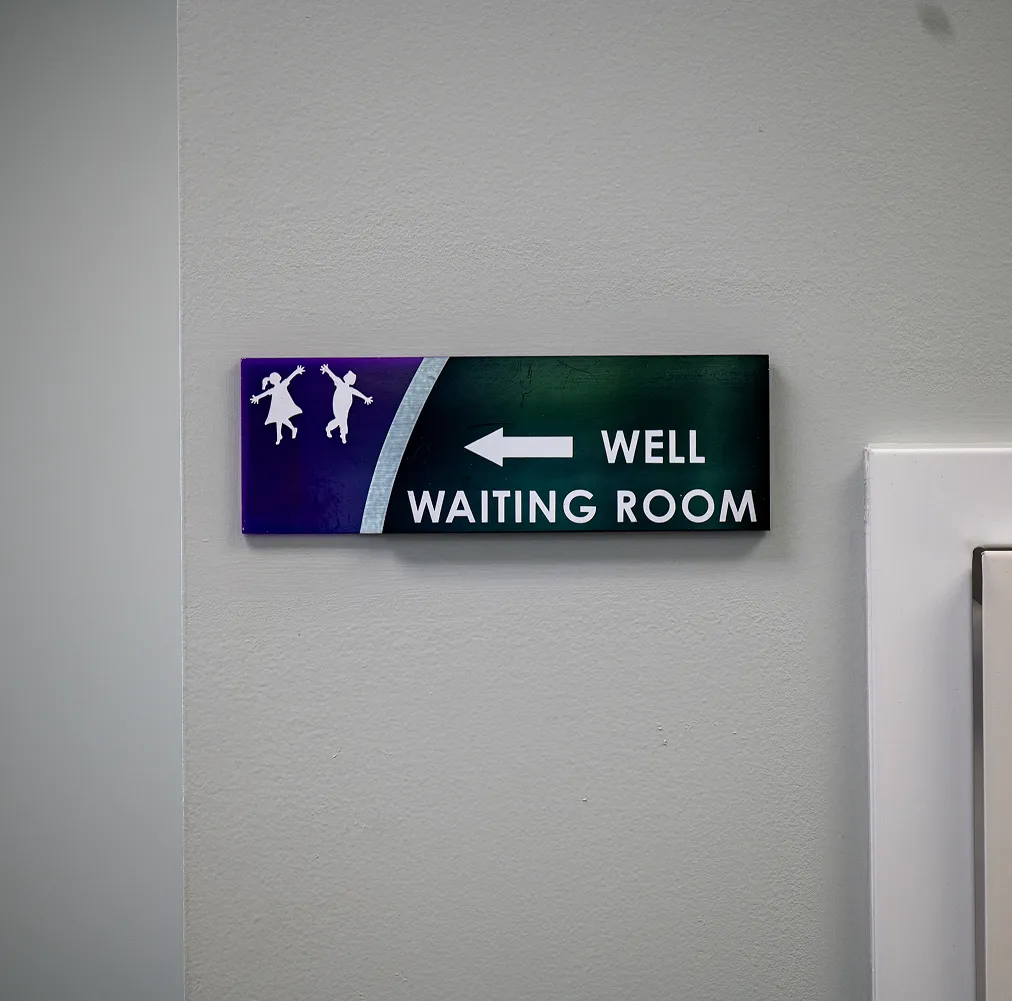 Wall sign with silhouettes of a girl and boy jumping, arrow pointing left, and text 'WELL WAITING ROOM'.