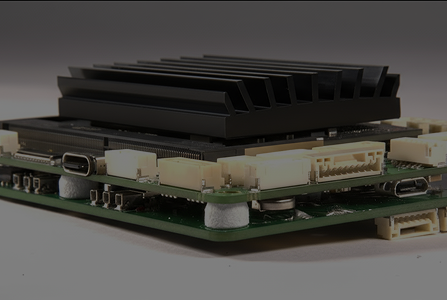 Close-up of a green circuit board with black heat sink and multiple white connectors on a gray background.