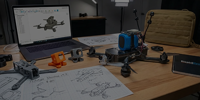 Desk with drone parts, technical sketches, and a laptop displaying a 3D drone model in a CAD program.