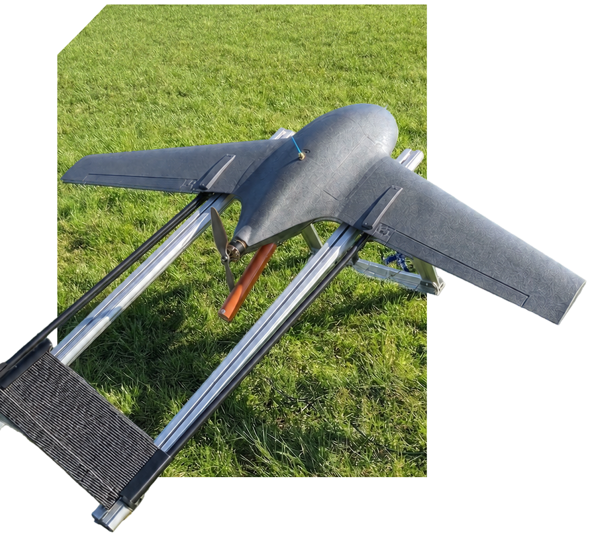 Small black drone plane with propeller on a metal launch rail over grass.