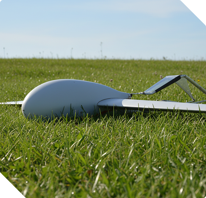 White drone with a solar panel lying on green grass under a clear blue sky.
