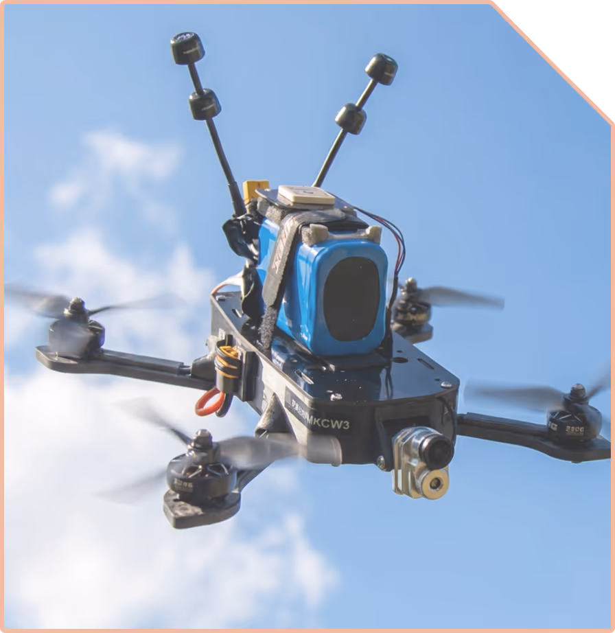 Close-up of a camera-equipped quadcopter drone flying against a blue sky with some clouds.